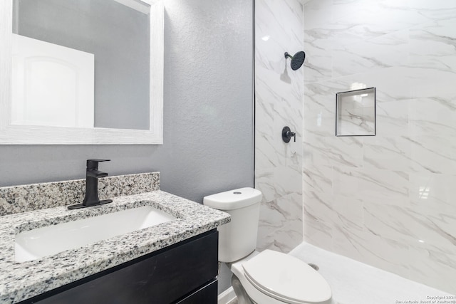 bathroom featuring a tile shower, vanity, and toilet