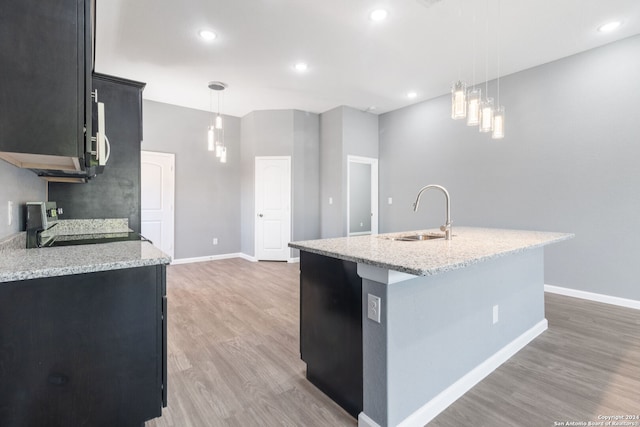 kitchen featuring an island with sink, light stone counters, sink, hanging light fixtures, and black range