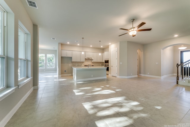 unfurnished living room with a healthy amount of sunlight, sink, light tile patterned floors, and ceiling fan