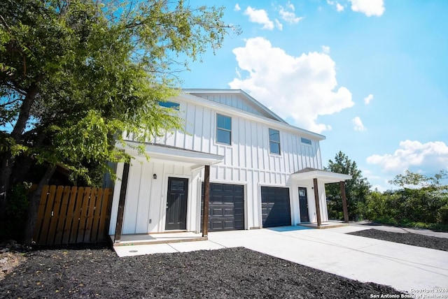 view of front facade featuring driveway, an attached garage, board and batten siding, and fence