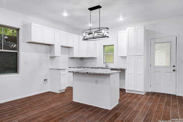 kitchen with dark wood-type flooring, a kitchen island, light stone counters, and a wealth of natural light