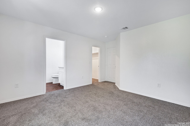 unfurnished bedroom featuring ensuite bathroom, a spacious closet, and dark carpet