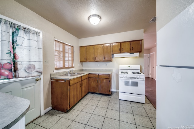 kitchen with white appliances, sink, light tile patterned floors, and a textured ceiling