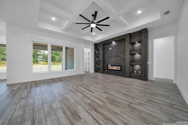 unfurnished living room featuring ceiling fan, hardwood / wood-style flooring, beamed ceiling, a tile fireplace, and coffered ceiling