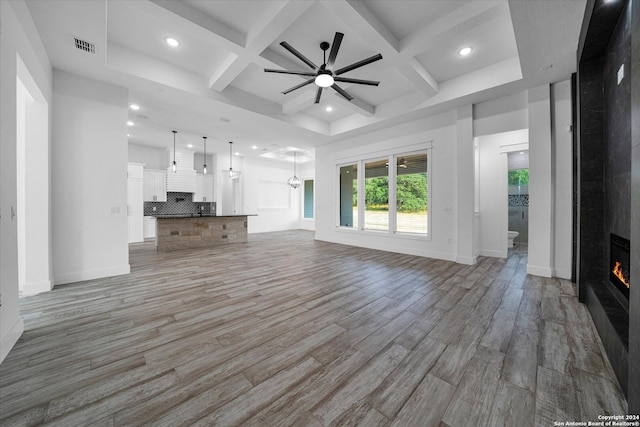 unfurnished living room featuring coffered ceiling, hardwood / wood-style flooring, beamed ceiling, a large fireplace, and ceiling fan