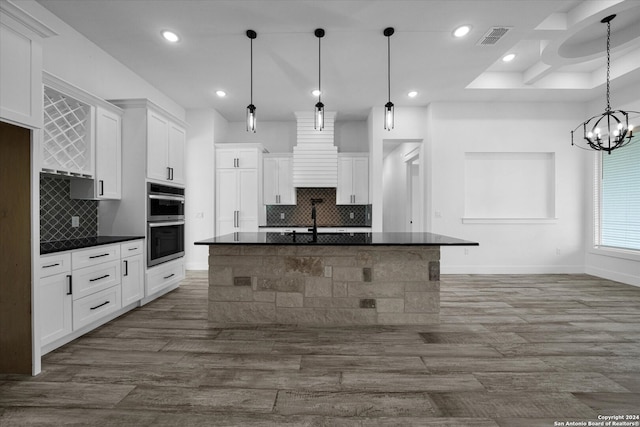 kitchen with white cabinets, hardwood / wood-style flooring, an island with sink, and hanging light fixtures