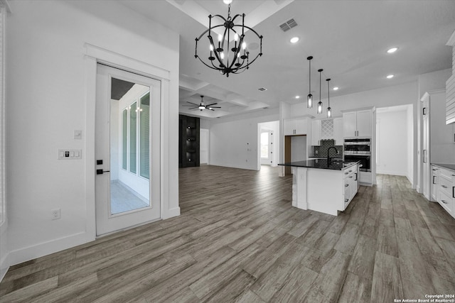 kitchen featuring double oven, a center island with sink, hardwood / wood-style floors, pendant lighting, and white cabinets