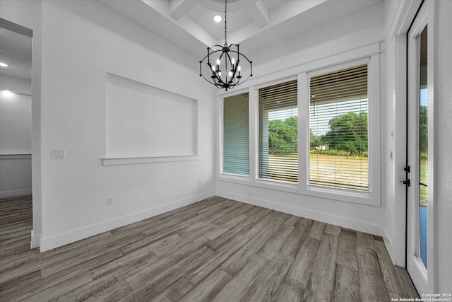 unfurnished dining area with beam ceiling, coffered ceiling, a notable chandelier, and wood-type flooring