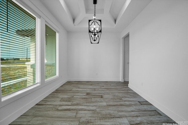 unfurnished dining area with a chandelier, a tray ceiling, and light wood-type flooring