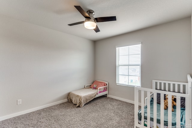 carpeted bedroom featuring a nursery area and ceiling fan