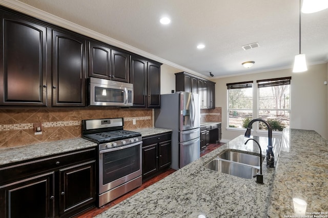 kitchen featuring stainless steel appliances, a sink, light stone counters, decorative light fixtures, and ornamental molding