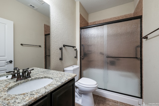 bathroom featuring tile patterned floors, toilet, vanity, a textured ceiling, and walk in shower