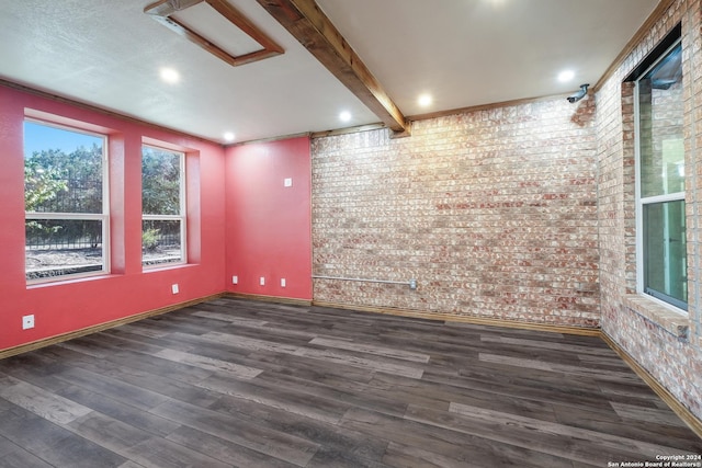 empty room with brick wall, baseboards, beam ceiling, and wood finished floors