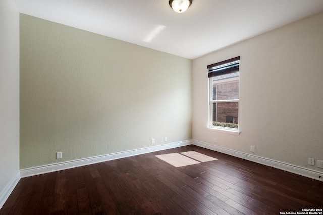 spare room with baseboards and dark wood-style flooring