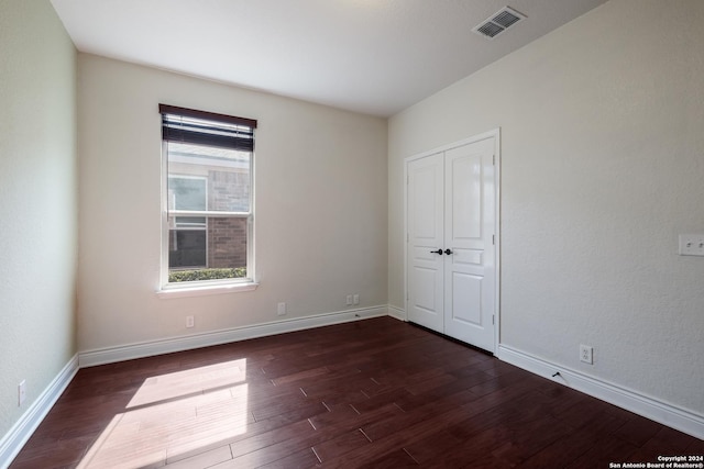unfurnished bedroom featuring visible vents, baseboards, dark wood-style floors, and a closet