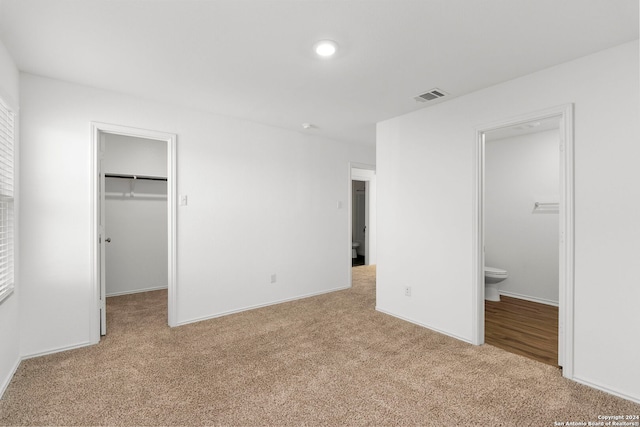 unfurnished bedroom with light colored carpet, connected bathroom, a closet, and a walk in closet