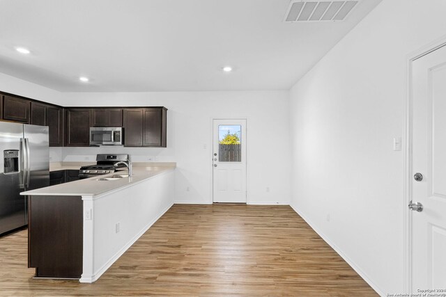 kitchen featuring kitchen peninsula, dark brown cabinets, sink, light wood-type flooring, and appliances with stainless steel finishes