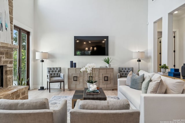 living room with light hardwood / wood-style floors, crown molding, a towering ceiling, and a fireplace