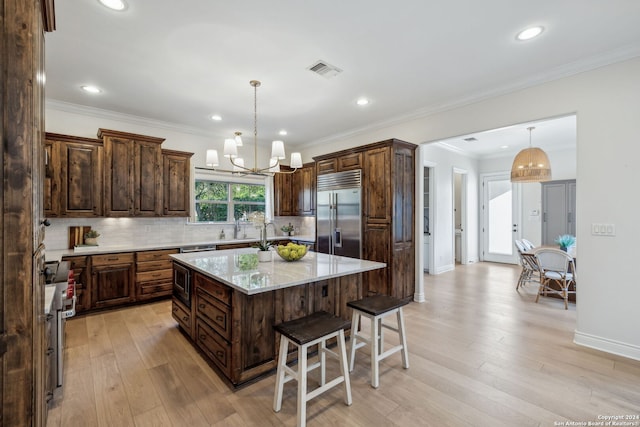 kitchen featuring a center island with sink, hanging light fixtures, light stone countertops, built in appliances, and light hardwood / wood-style floors