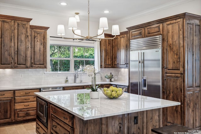 kitchen with light stone countertops, a kitchen island, decorative light fixtures, built in appliances, and a notable chandelier