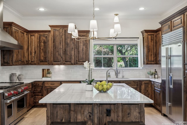 kitchen featuring wall chimney exhaust hood, a center island, dark brown cabinetry, and premium appliances