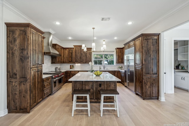 kitchen with light hardwood / wood-style flooring, wall chimney exhaust hood, a kitchen island, and high end appliances