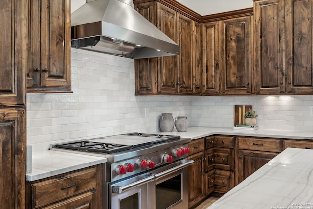 kitchen featuring range with two ovens, dark brown cabinets, wall chimney range hood, and decorative backsplash