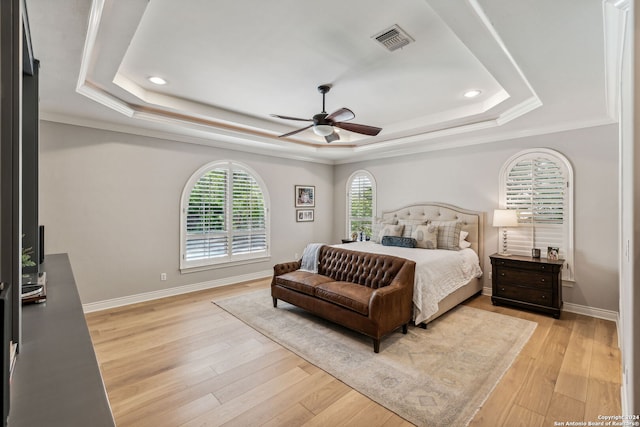 bedroom with light hardwood / wood-style floors, a tray ceiling, and ceiling fan