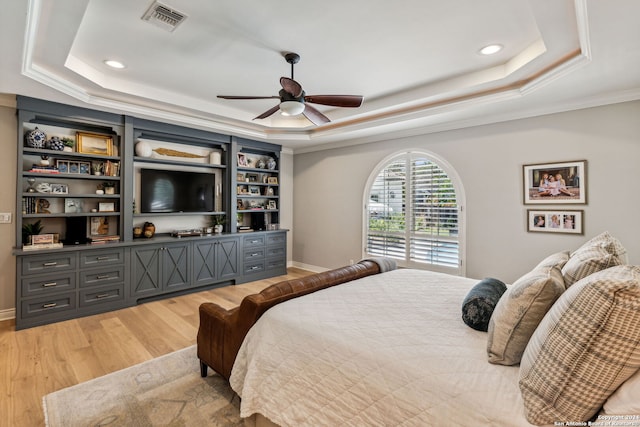 bedroom with crown molding, light hardwood / wood-style flooring, a tray ceiling, and ceiling fan