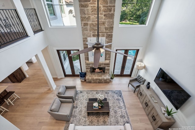 living room featuring light hardwood / wood-style floors, a stone fireplace, a towering ceiling, and ceiling fan