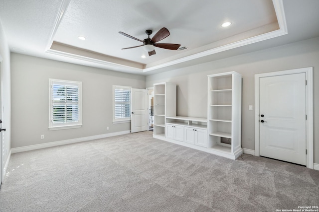 unfurnished living room featuring crown molding, ceiling fan, light carpet, and a raised ceiling