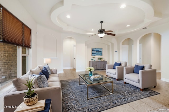 tiled living room with arched walkways, a tray ceiling, visible vents, a ceiling fan, and baseboards