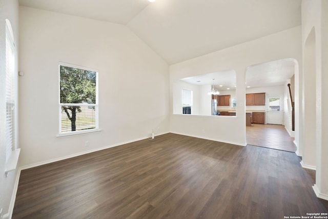 unfurnished living room with a chandelier, plenty of natural light, high vaulted ceiling, and dark wood-type flooring