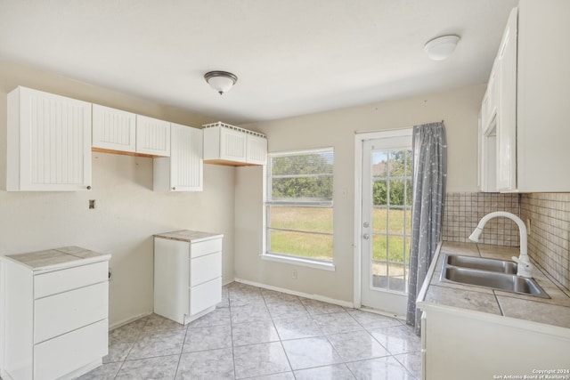 kitchen with decorative backsplash, tile counters, sink, light tile patterned floors, and white cabinetry