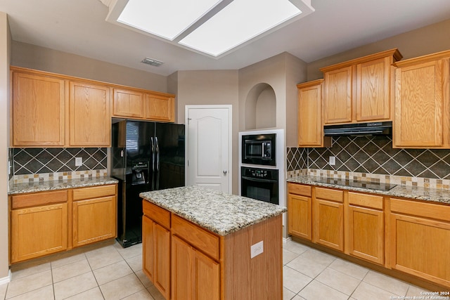 kitchen with decorative backsplash, a kitchen island, light stone countertops, light tile patterned flooring, and black appliances