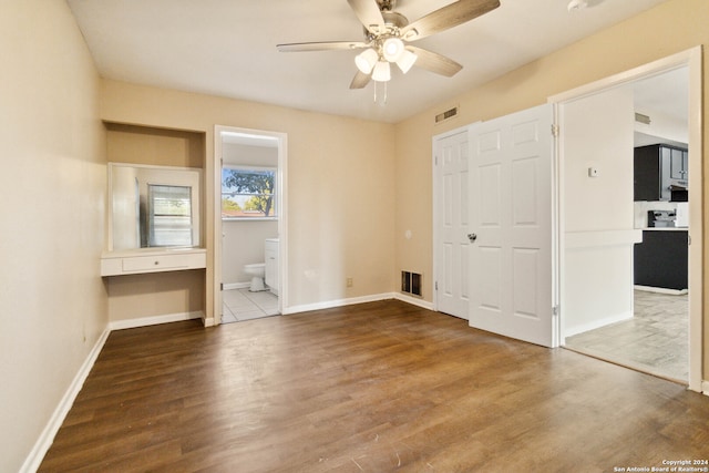 unfurnished bedroom featuring a closet, ensuite bath, wood-type flooring, and ceiling fan