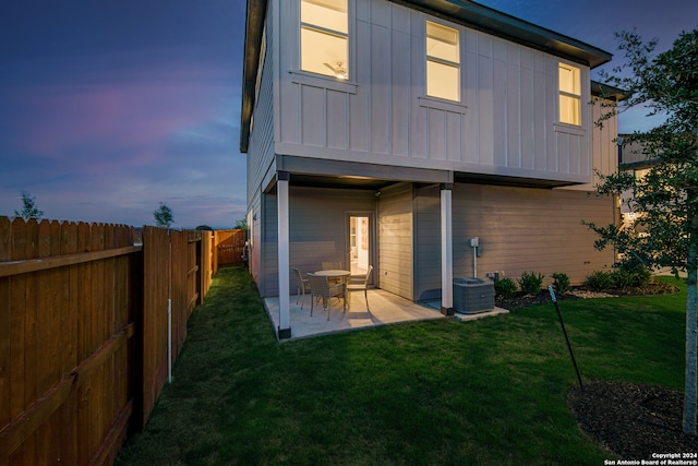 back house at dusk featuring a patio area, central AC, and a lawn