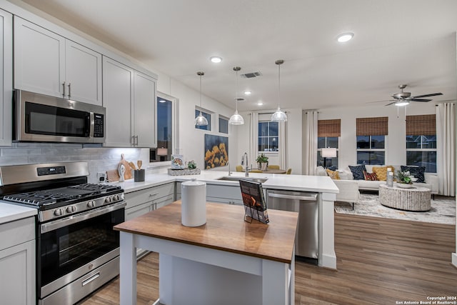 kitchen with hanging light fixtures, appliances with stainless steel finishes, dark hardwood / wood-style floors, sink, and a center island