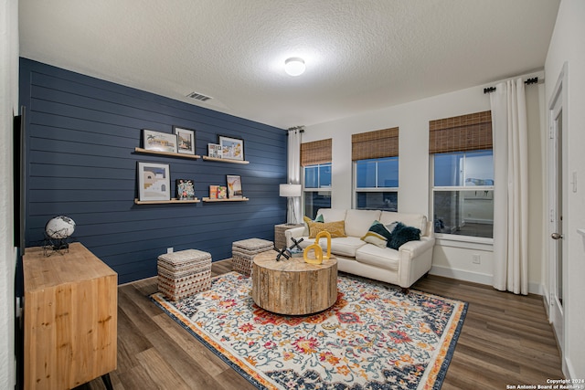 living room with a textured ceiling, dark hardwood / wood-style floors, and wooden walls