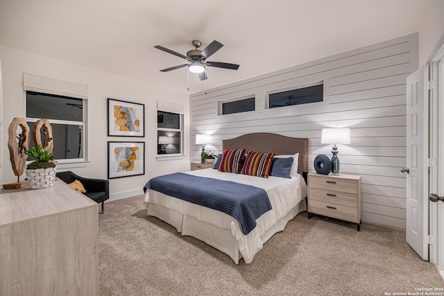 bedroom featuring wooden walls, light colored carpet, and ceiling fan