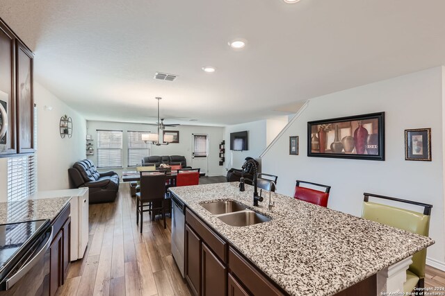 kitchen with sink, light wood-type flooring, an island with sink, dark brown cabinetry, and stainless steel dishwasher