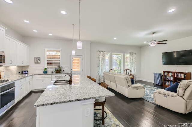 kitchen with appliances with stainless steel finishes, white cabinetry, a kitchen bar, dark hardwood / wood-style floors, and sink