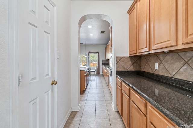 kitchen featuring dark stone counters, light tile patterned flooring, pendant lighting, a textured ceiling, and tasteful backsplash