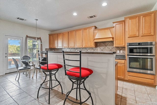 kitchen featuring tasteful backsplash, a kitchen breakfast bar, premium range hood, pendant lighting, and double oven