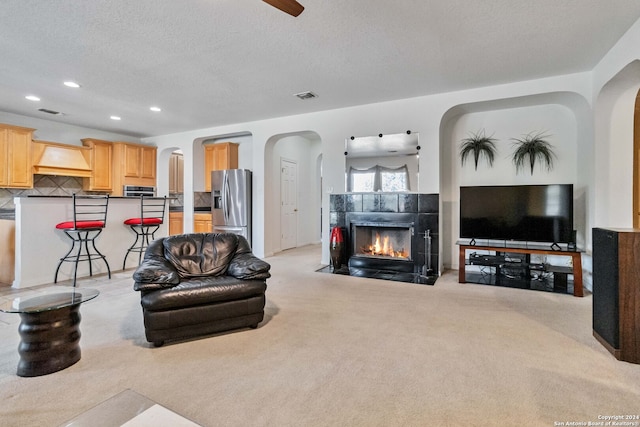 carpeted living room with a tiled fireplace, a textured ceiling, and ceiling fan