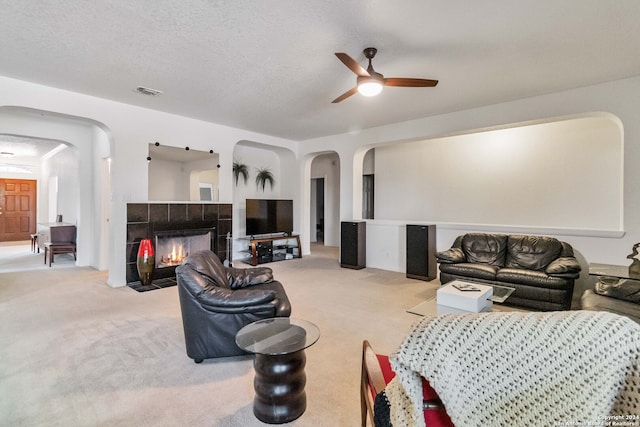 carpeted living room with a textured ceiling, a tiled fireplace, and ceiling fan