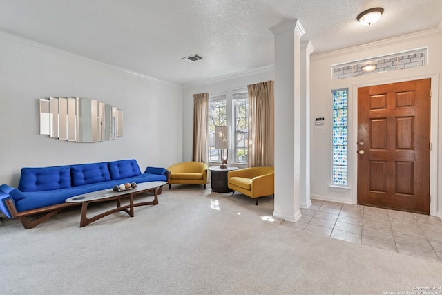 carpeted foyer entrance with ornamental molding, a textured ceiling, and decorative columns