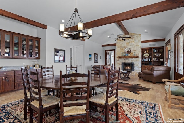 dining space featuring light hardwood / wood-style floors, a stone fireplace, beam ceiling, ceiling fan with notable chandelier, and high vaulted ceiling