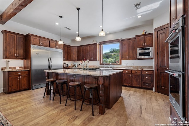 kitchen featuring appliances with stainless steel finishes, a center island, a kitchen breakfast bar, light hardwood / wood-style floors, and decorative light fixtures