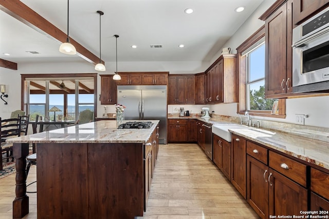 kitchen with a kitchen island, light hardwood / wood-style floors, stainless steel appliances, decorative light fixtures, and light stone counters